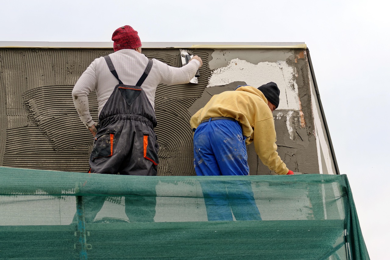 Workers applying plaster to an exterior wall during repair